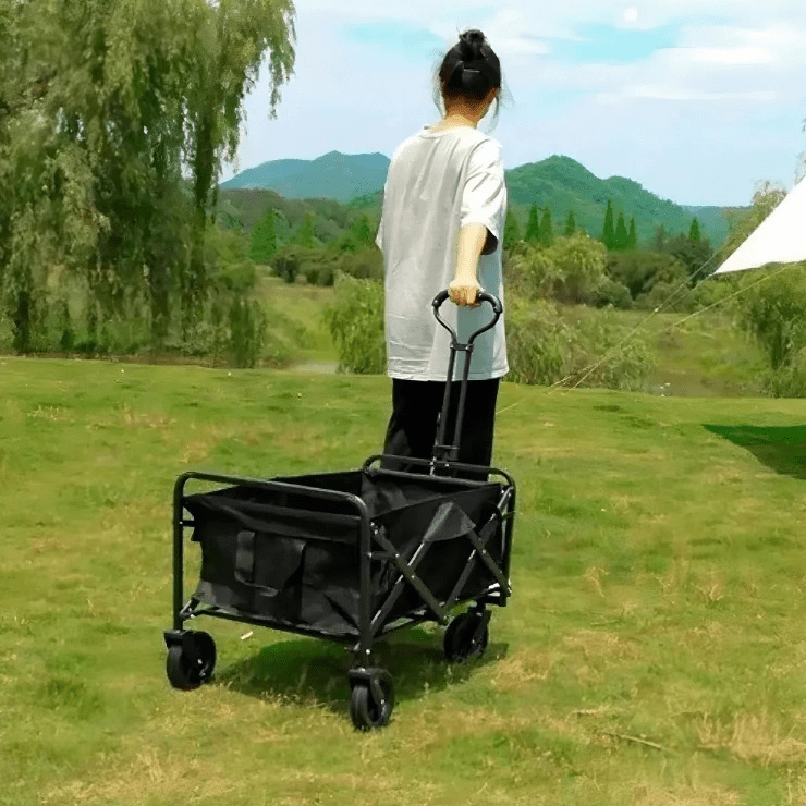 Mujer jalando carrito plegable negro en campo verde